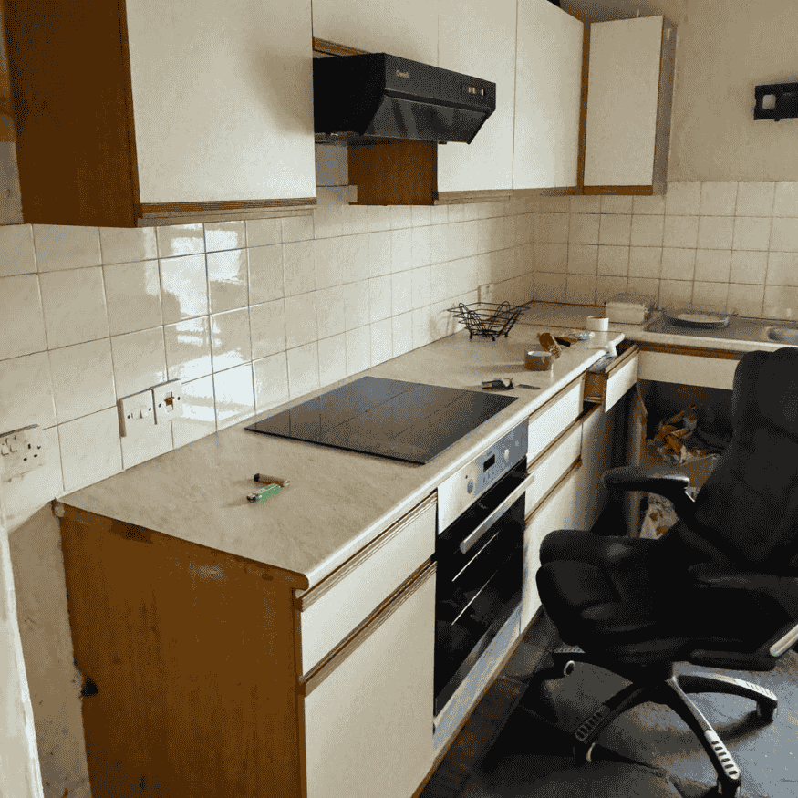 Outdated kitchen interior prior to refurbishment, featuring worn countertops, disused cabinets, and unclean flooring.