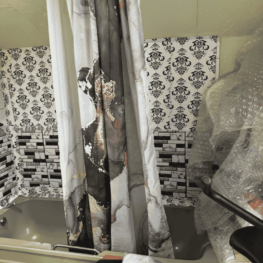 Old-fashioned bathroom needing landlord property refurbishment in Northampton, with stained shower curtain, damaged tiles, and outdated fittings.